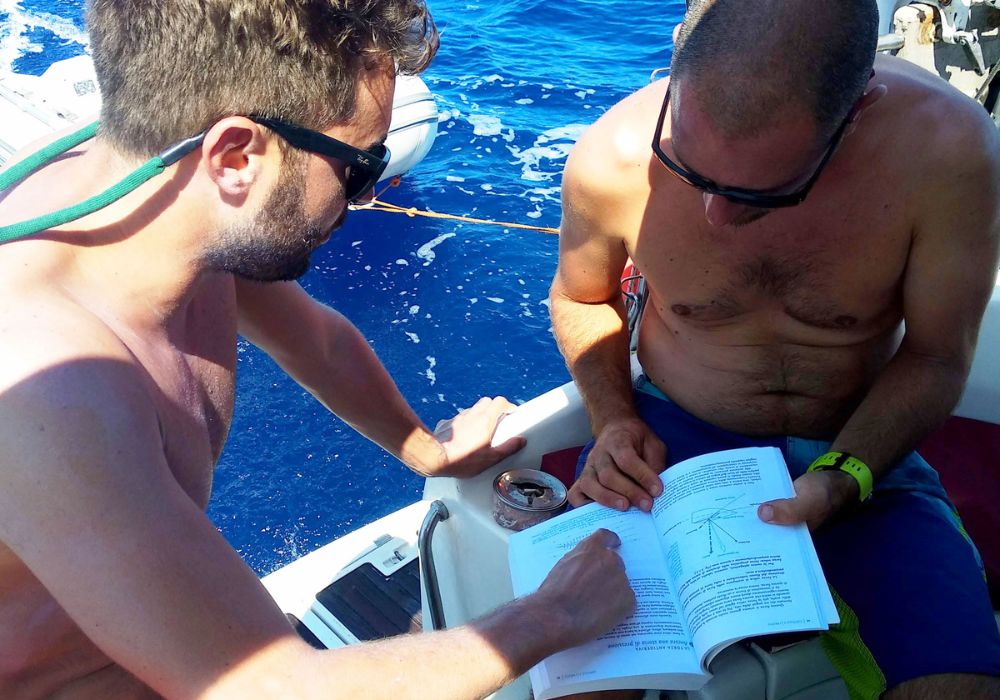 Foto di due ragazzi che leggono un manuale di vela in barca
