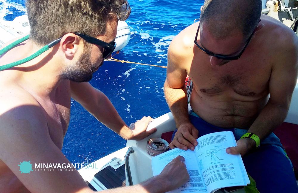 Andrea, lo skipper di Mina Vagante 2, insieme a un ospite che leggono un manuale di vela
