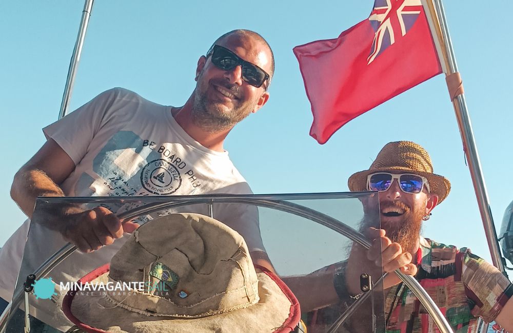 Foto dello skipper di Mina Vagante 2 che conduce la barca con un ospite sorridente accanto